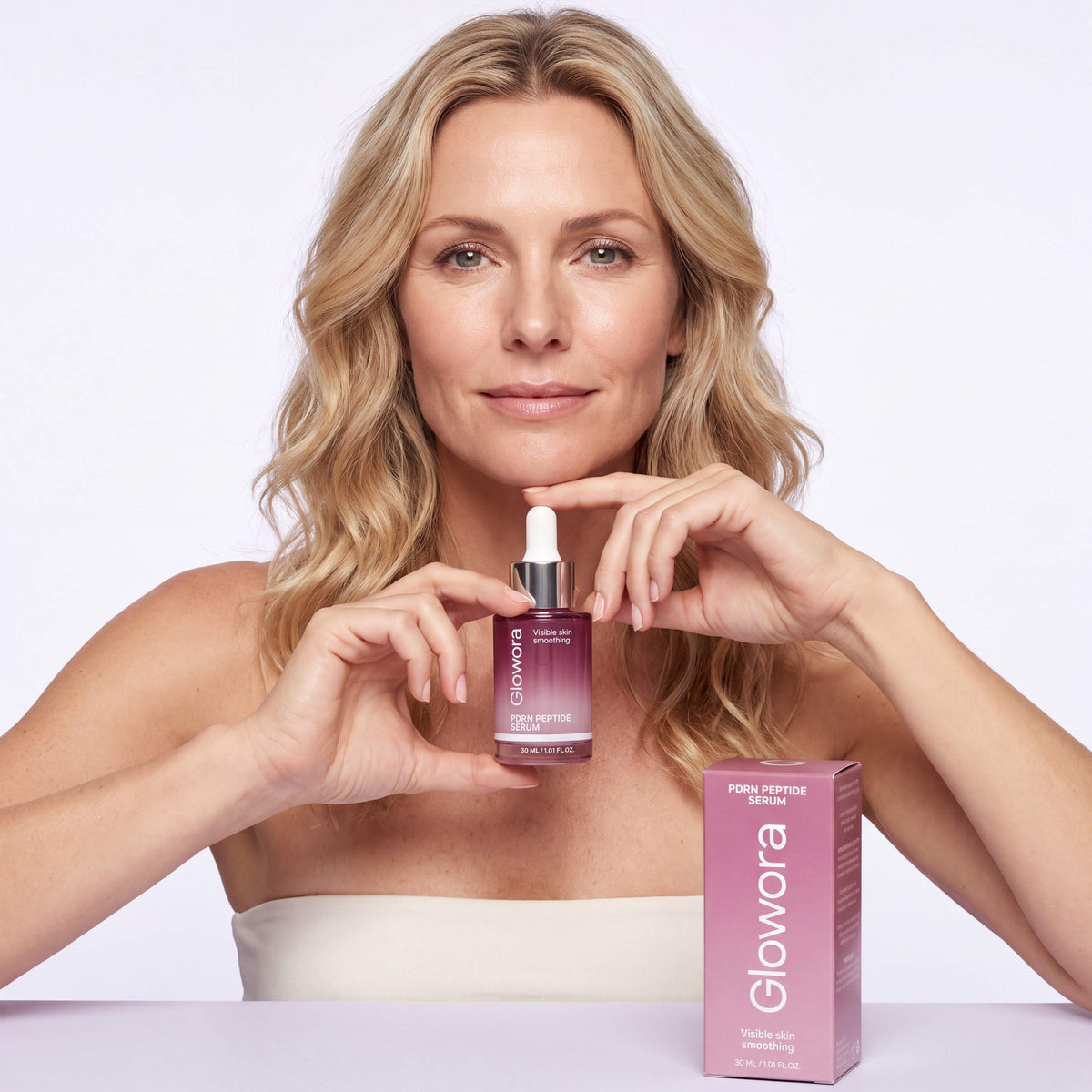 Vrouw houdt PDRN Peptide Serum flesje onder haar kin naast de roze doos