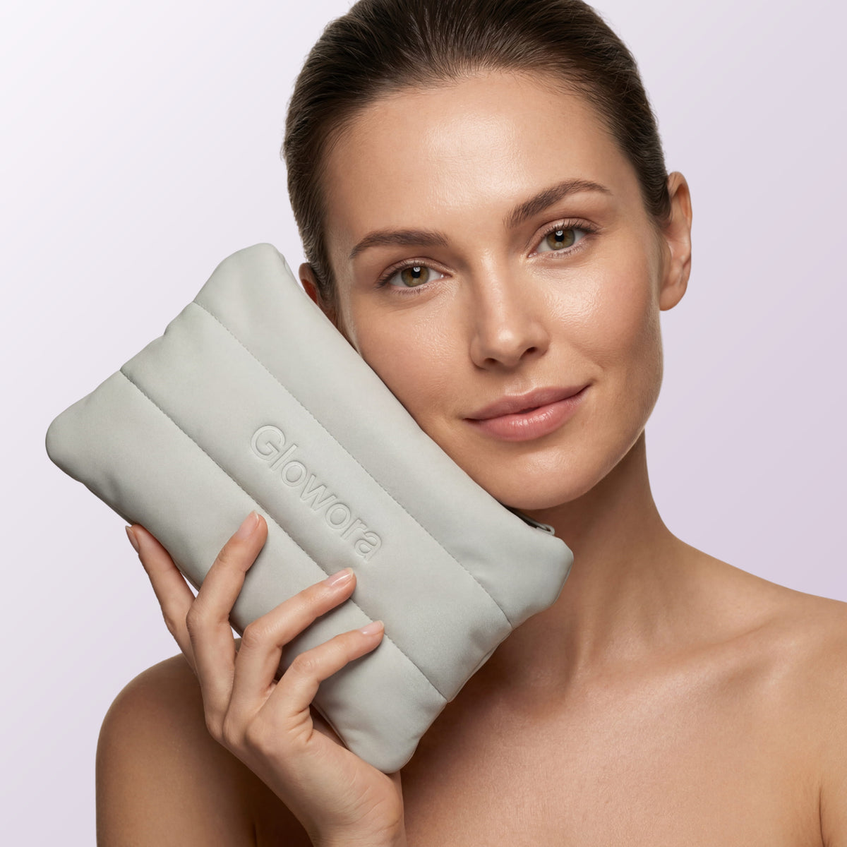 Vrouw houdt de grijze gewatteerde Ritual Pouch met Glowora-logo tegen haar gezicht